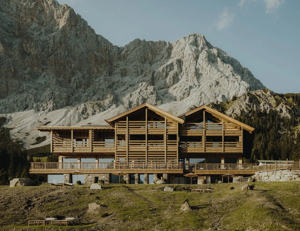 eriro Alpine Hide in golden afternoon sun with twin gables, larch wood terrace balconies and natural stone base before Wetterstein massif