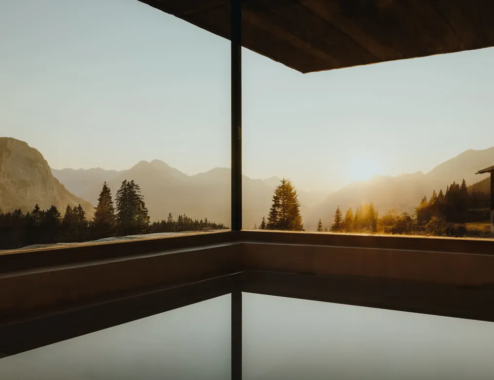 Infinity pool at eriro with overflow edge toward sunset over Wetterstein and Mieminger ranges, mirroring water surface beneath dark wood ceiling