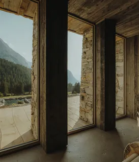 Wellness room at eriro with stacked stone walls, reclaimed wood ceiling, sauna bucket and panorama window to natural bathing pond and Wetterstein summits