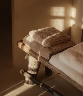 Soft towels in taupe and cream on rustic wooden bench in warm light – luxurious spa sanctuary at eriro Alpine Hide