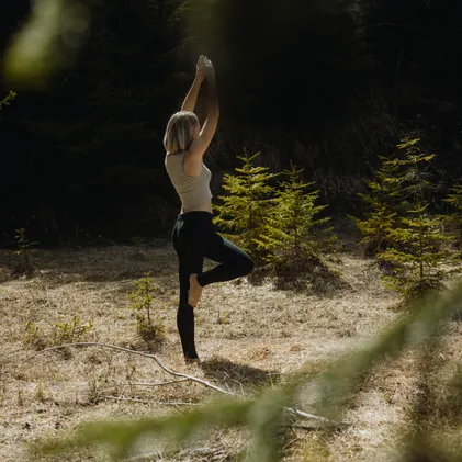 Woman in tree pose during yoga on sunny forest clearing surrounded by young spruces – outdoor yoga experience at eriro Alpine Hide retreat