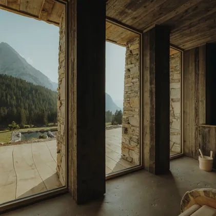 Wellness room at eriro with stacked stone walls, reclaimed wood ceiling, sauna bucket and panorama window to natural bathing pond and Wetterstein summits