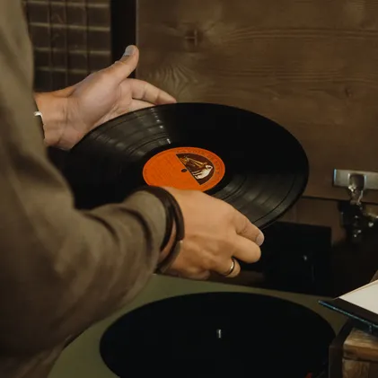 Hands placing vintage vinyl record on turntable at eriro Alpine Hide – analog moments of indulgence in warm wood atmosphere
