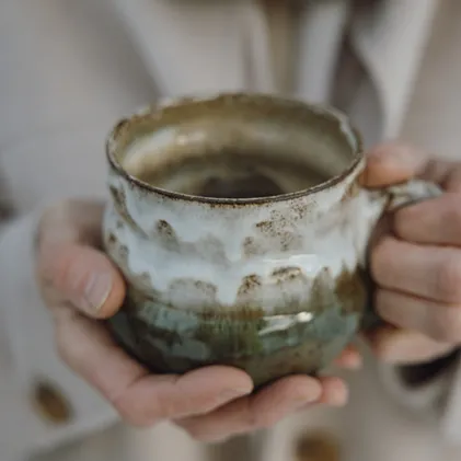 Hand-thrown ceramic cup with gradient glaze in white and moss green – gently cradled as warming moment of indulgence at eriro alpine resort