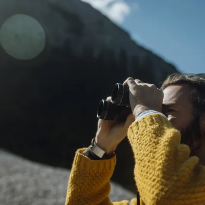 Man in mustard knit sweater observing intently through binoculars the summits of Mieminger mountain range from eriro Alpine Hide panorama