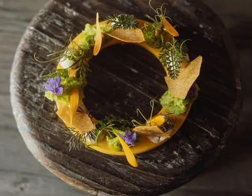Artfully circular plated dish with edible flowers and herbs on weathered wooden block – alpine eriro fine-dining culinary art