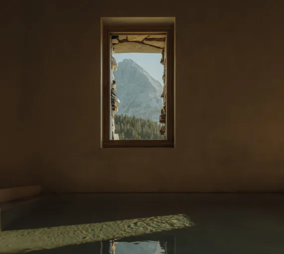 Vertical window in eriro spa framing Wetterstein summits above spruce forest, dark plunge pool mirroring mountain light in hand-plastered ochre clay wall