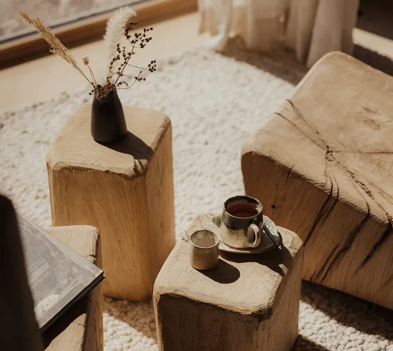 Solid wood side tables of hand-carved tree trunks with ceramic cup and dried grasses at eriro Alpine Hide – warm alpine living culture