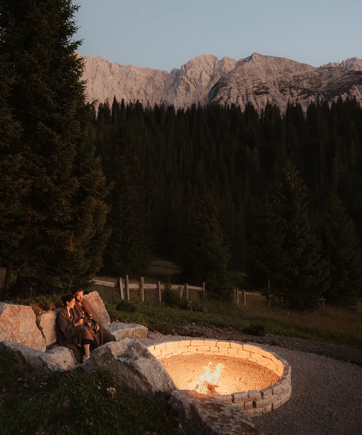 Couple enjoying evening at fire pit before imposing alpine backdrop – romantic togetherness at eriro Alpine Hide at dusk