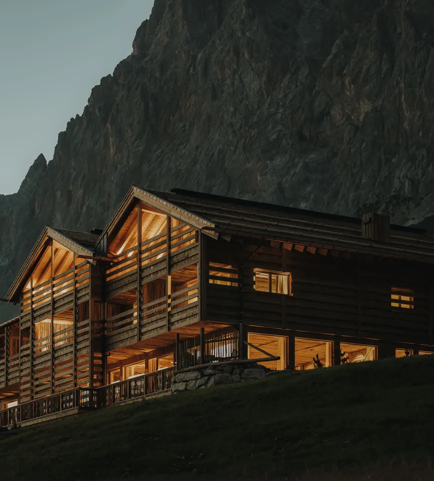 eriro Alpine Hide at dusk with golden-lit larch loggias and horizontal wood slats before shadowy Wetterstein massif on alpine slope